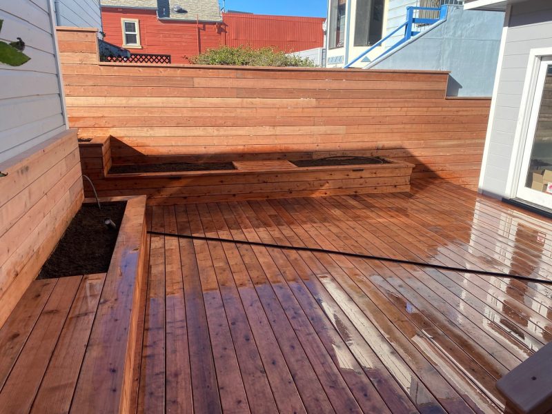 Completed deck in foreground with raised planters to left of deck. Another raised planter in back of deck against redwood fence.