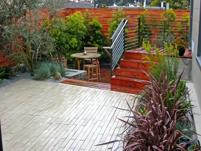 redwood stairs lead to a stone patio, which then leads to another lower level with built in planter and trees