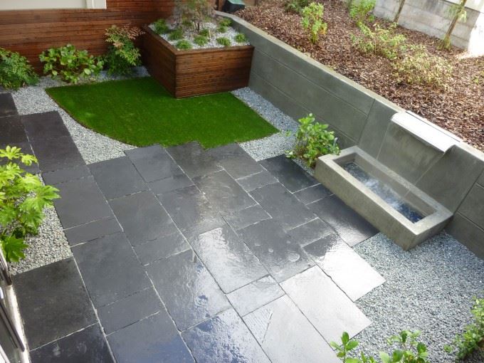 Black limestone patio with artificial turf on top left corner. Stainless steel weir waterfall on right back of patio.