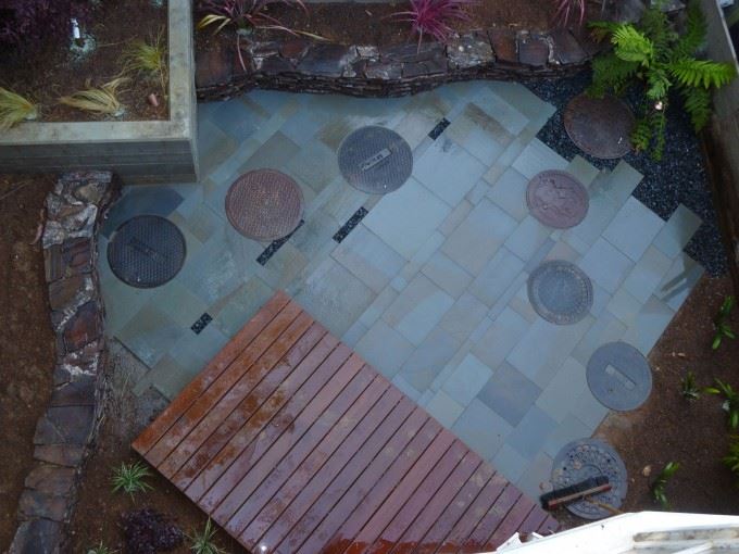 Freeform round bluestone patio embedded with six manhole covers in different colors.