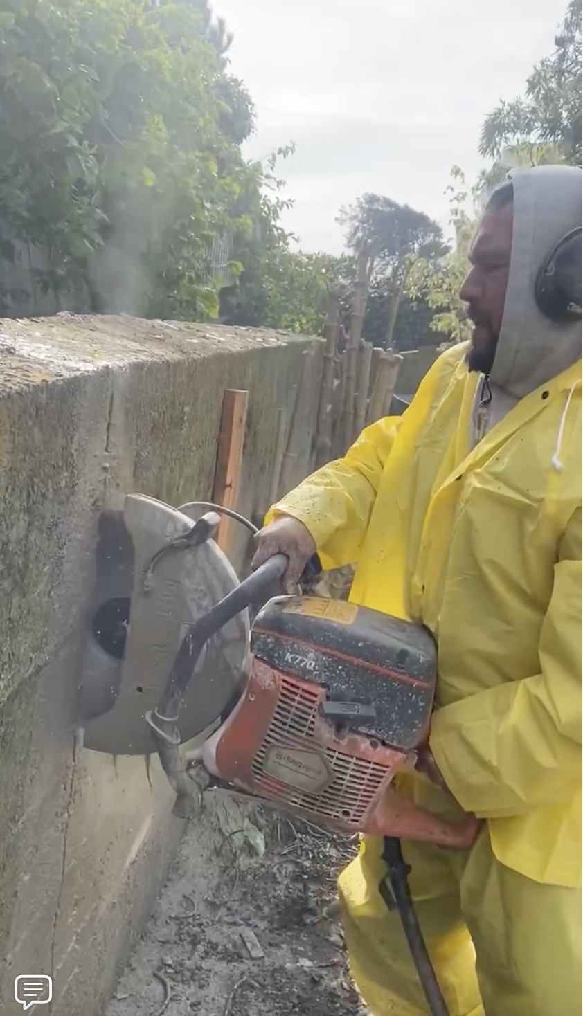 Demo of client's retaining wall using concrete saw held by worker in yellow protective suit.