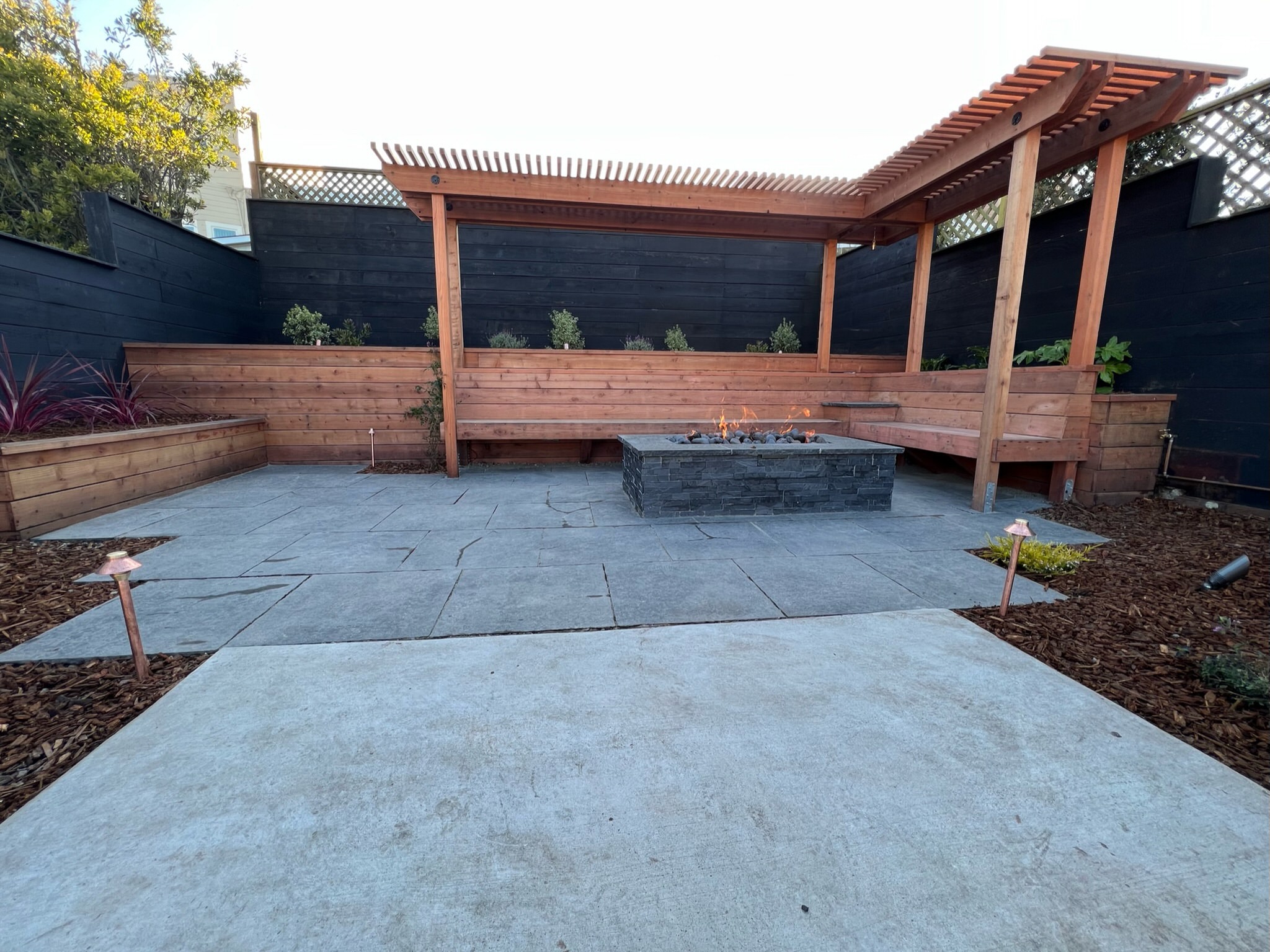 Completed redwood bench, pergola, and fire pit at our Outer Sunset, San Francisco project. Black basalt patio.