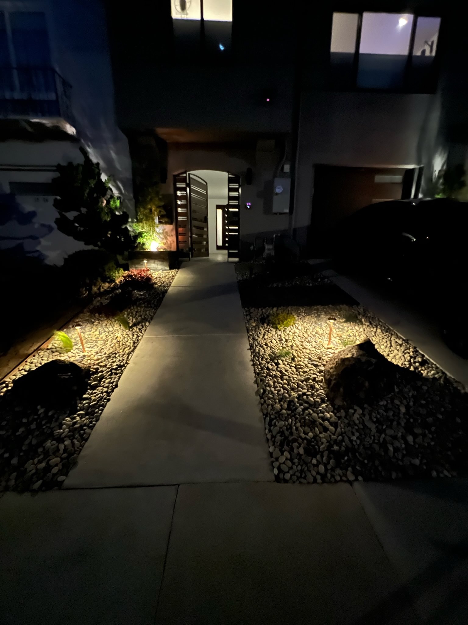 Completed front yard at night. New landscape on left and right side of concrete walkway. One boulder on each side in front surrounded by Lynn Creek.