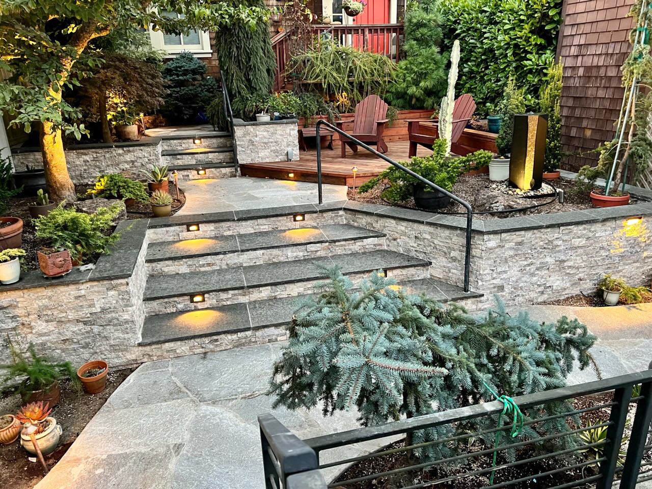 Completed black basalt stairs, quartzite flagstone walkway, retaining walls faced with silver travertine, and redwood deck.