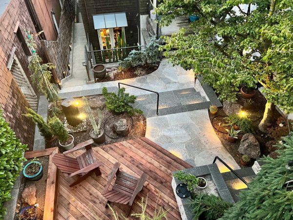 Birds eye view of our client's completed backyard hardscaping make-over. Redwood deck in left foreground, black basalt stairs in middle, quartzite flagstone walkway to left of deck and below stairs, planters to the right and left of deck, and retaining walls.