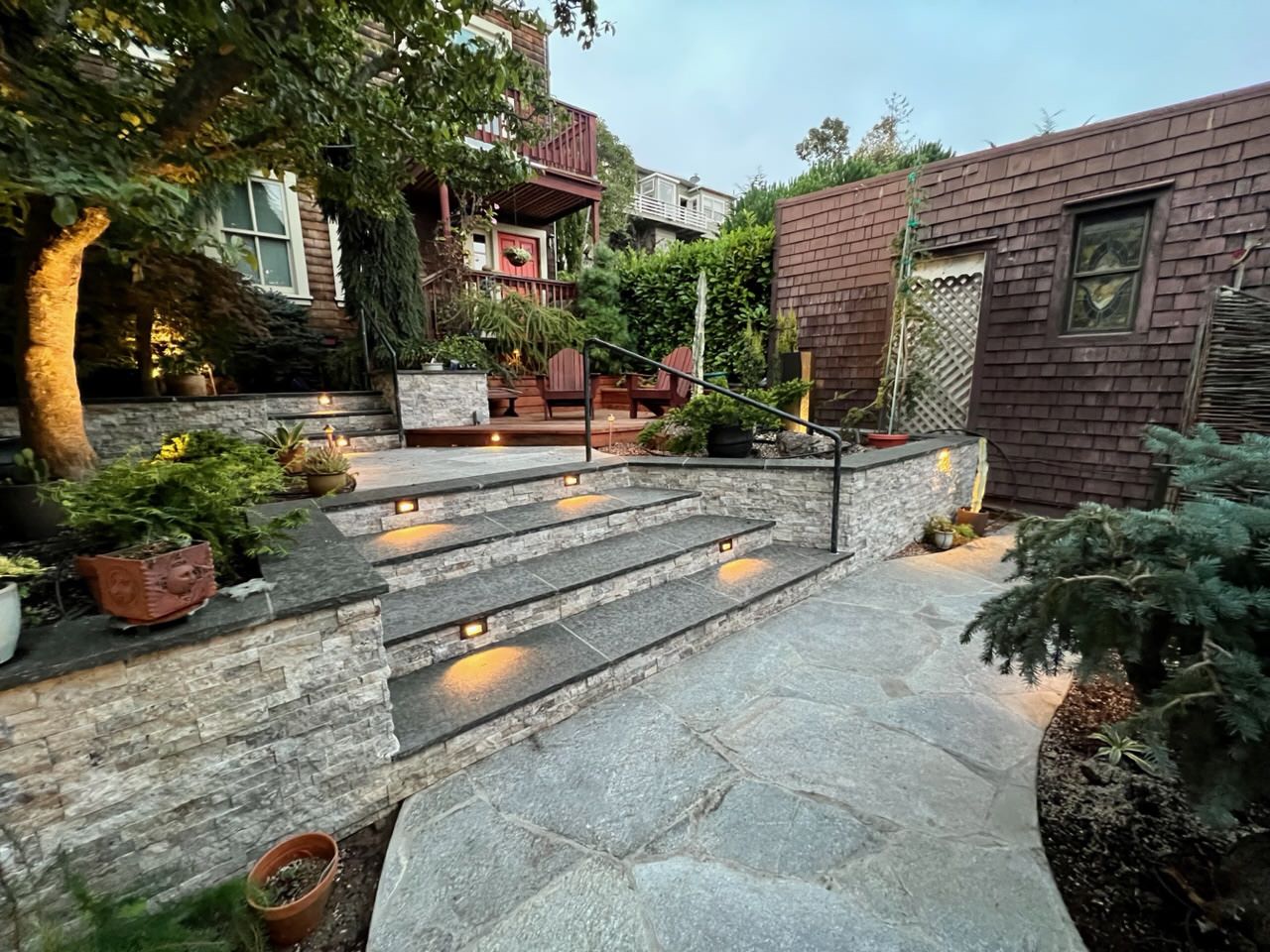 Completed black basalt stairs, quartzite flagstone walkway, retaining walls faced with silver travertine, and redwood deck.