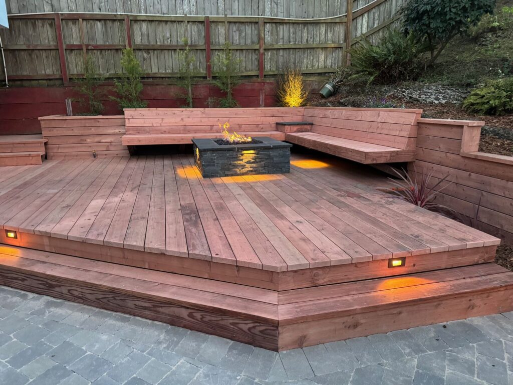 stone patio leads to a raised redwood deck with built in seating and a custom fire pit